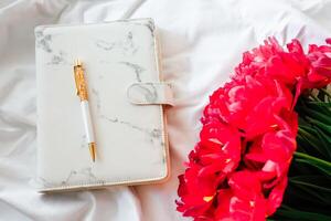 Elegant workspace setup with a marble notebook and vibrant flowers photo