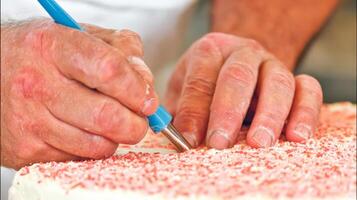 Close up of Baker's Hands Decorating a Birthday Cake with Red Sprinkles photo