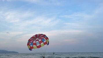 Man flying on parachute wide shot top view. Parachute flying over water with mountains on background. Parasailing in sea across seaside. video
