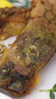 Two pieces of fried carp Fried tail portion and other slices of carp decorated with lemon slices on a white dish on the rustic table, top view while rotation video