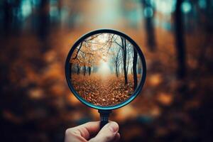 Hand holding magnifying glass showing autumn forest path photo