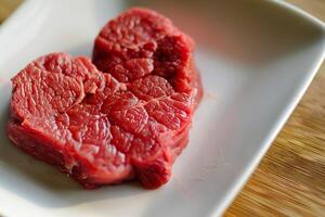 Raw beef steak lying on white square plate on wooden table photo