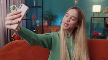 Happy girl blogger taking selfie on smartphone communicating call home online with subscribers video