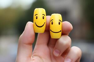 Two small yellow cylinders with happy faces are being held up by a hand photo