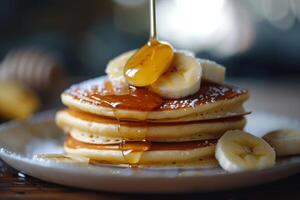 Stack of pancakes with banana slices and icing sugar, honey being poured on a plate photo