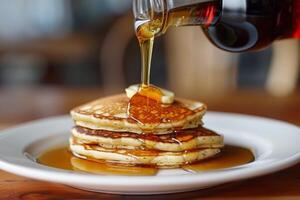 Pouring maple syrup on stack of pancakes with butter for breakfast photo