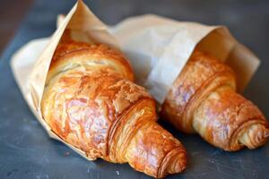 Two freshly baked croissants wrapped in brown paper on dark surface photo