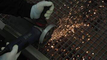 Construction worker cutting metal surface with angle grinder creating bright flying sparks, close-up view of gloved hands operating power tool in industrial workshop environment video