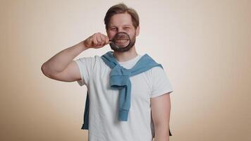 Caucasian man holding magnifier glass on teeth, looking at camera showing funny smiling face mouth video