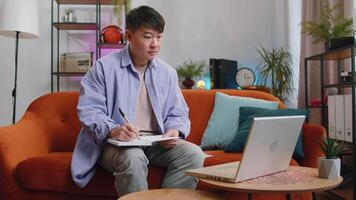 Asian handsome man at home making conference call talking to webcam, making notes on notebook video