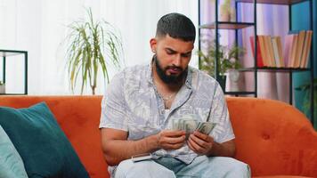 Rich happy Indian man counting money cash on smartphone calculator app, calculate income earnings video