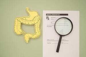 Top view of an intestine symbol made from yellow paper and a magnifying glass over the medical prescription on a green background. photo