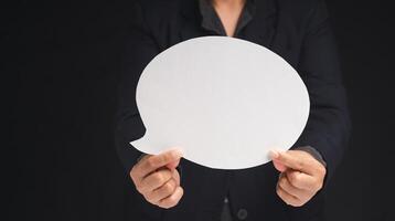 Close-up of a businessman holding a blank white speech bubble while standing on a black background. Space for text. photo