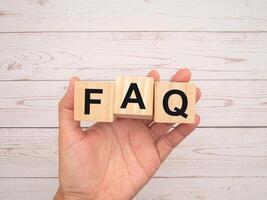 FAQ. Frequently asked questions. Wooden cubes with the letters F, A, and Q in hand over a wooden table photo