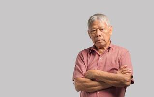 Senior man looking at the camera with a smile and arms crossed while standing on a gray background. Space for text. photo