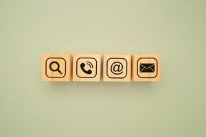 Top view of wooden cubes with symbols of a magnifying glass, mobile, address, and email on a green background. Flat Lay. photo