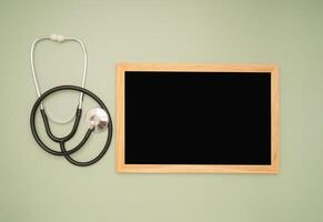 Top view of a stethoscope and a blank mini chalkboard on a green background photo