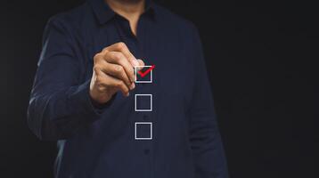 Businessman holding a pen and checking a mark on the boxes symbol is one of three options while standing on a black background photo