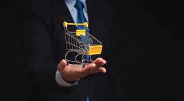 Businessman in a suit with a mini shopping trolley in hand while standing on a black background photo