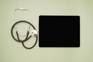 Top view of a stethoscope and a blank screen tablet on a green background photo