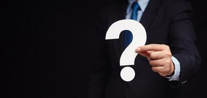 Close-up of a businessman holding a white question mark paper while standing on a black background. photo