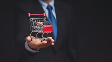 Close-up of a businessman in a suit with a mini shopping trolley in hand while standing on a black background. photo