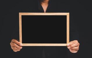 Close-up of hands holding a blank mini chalkboard while standing on a black background photo