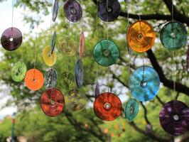Colorful glass discs hang from a tree, creating a whimsical decoration against a lush green backdrop. photo