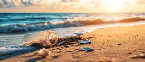 A glass jar lies on the beach shore, partially submerged in water, with gentle waves and a serene sunset in the background. photo