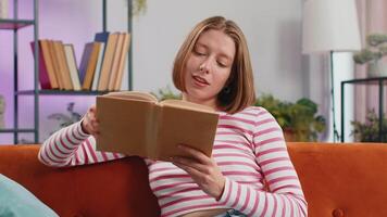 Young woman relaxing interesting book turning pages smiling enjoying literature taking rest on sofa video