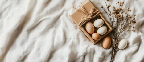 A rustic arrangement featuring a box of eggs alongside dried flowers on a textured fabric background. photo