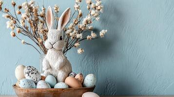 A decorative Easter scene featuring a bunny figurine surrounded by pastel-colored eggs and floral accents against a textured blue background. photo