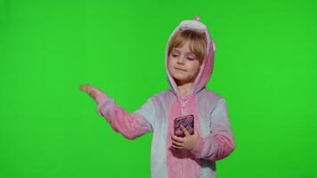 Child girl in unicorn pajama using, holding smartphone, pointing at something with hands, copy space video