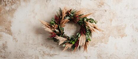 A decorative wreath made of dried plants and greenery, set against a textured wall background. photo