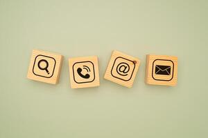 Top view of wooden cubes with symbols of a magnifying glass, mobile, address, and email on a green background photo