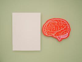 A blank white paper and a red brain shape symbol on a green background photo