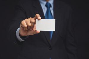 Businessman showing a blank white name card mockup while standing on a black background photo