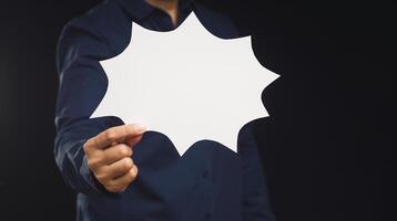 Businessman holding a blank white comic speech bubble while standing on a black background photo