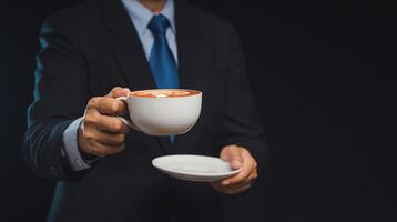 Close-up of a businessman in a suit is holding a cup of coffee while standing on a black background photo