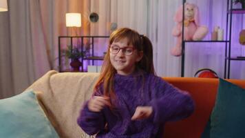 Happy toddler child girl dancing and moving to rhythm making trendy dub dance gesture at modern home video