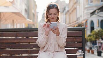 Young woman use smartphone typing text messages browsing internet finishing work looking at camera video