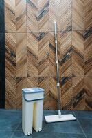 A mop and a bucket filled to the brim with clear water rest neatly on the polished floor before a beautifully crafted wooden wall, which enhances the rooms rustic charm and warmth photo