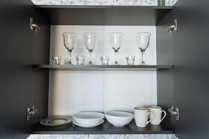 In a beautiful kitchen, there is a spacious cabinet that is filled to the brim with an assortment of plates, bowls, and delicate wine glasses, creating an inviting atmosphere for dining photo