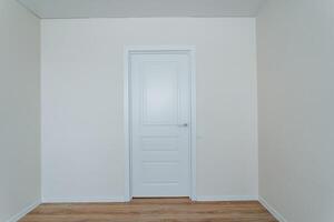 In the middle of the house, there exists an empty room which features a simple yet elegant white door alongside a charming wooden floor that enhances the overall appearance of the space photo