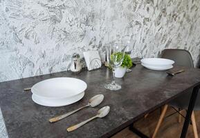 A beautifully set dining table adorned with dishes, utensils, glasses, and a lovely plant arrangement placed on it, creating an inviting atmosphere for meals and gatherings photo
