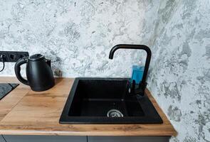 There is a kitchen sink equipped with a stylish black faucet, all beautifully set on a wooden counter top that adds a rustic charm to the space, enhancing the overall kitchen aesthetics photo