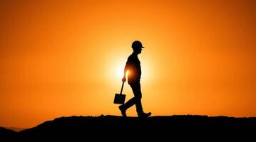 Silhouette of a construction worker walking against the sunset holding shovel photo