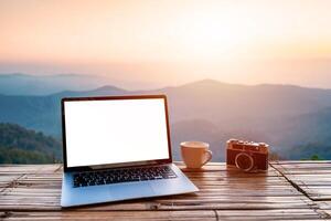 Empty screen laptop with cup of coffee and camera with mountain view at sunrise photo