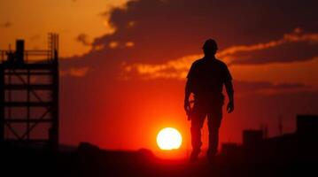 Silhouette of construction worker standing against the sunset sky photo