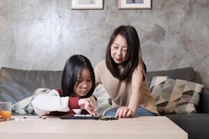 Asian single mum, and child fun playing Go, checkers board game on table in home living room together with love and cheerful, happy weekend relaxing hobby of family. photo